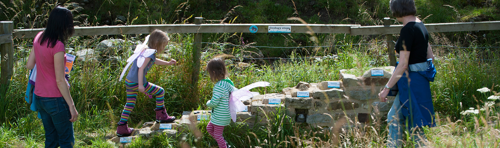 Two adults with two children wearing fairy wings and climbing up a step like stone structure