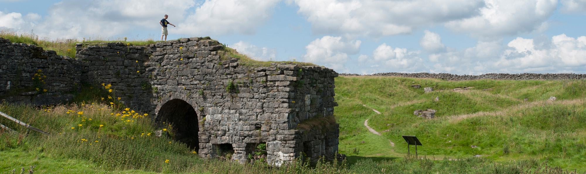 A person stood on top of remains of Toft Gate Lime Kiln, with an archway, and a green field to the right