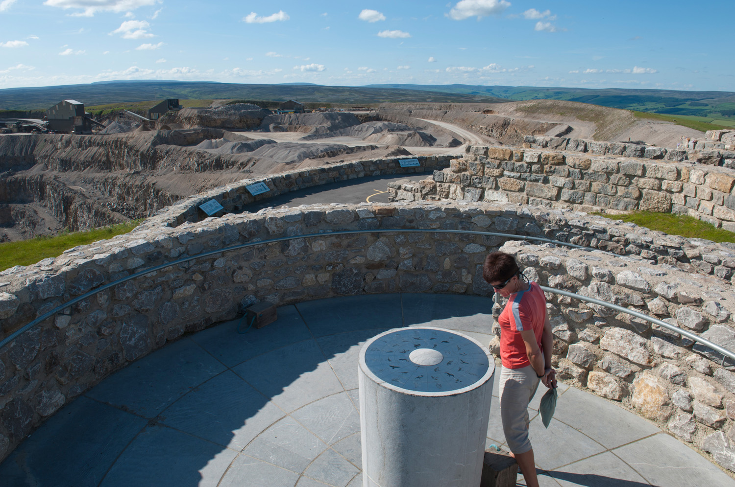 Woman looking at display surrounded by stone walls with countryside views in distance
