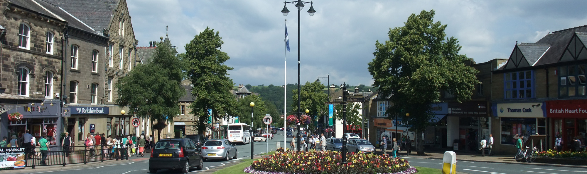 The town centre of Ilkley with people, shops, cars and a bus