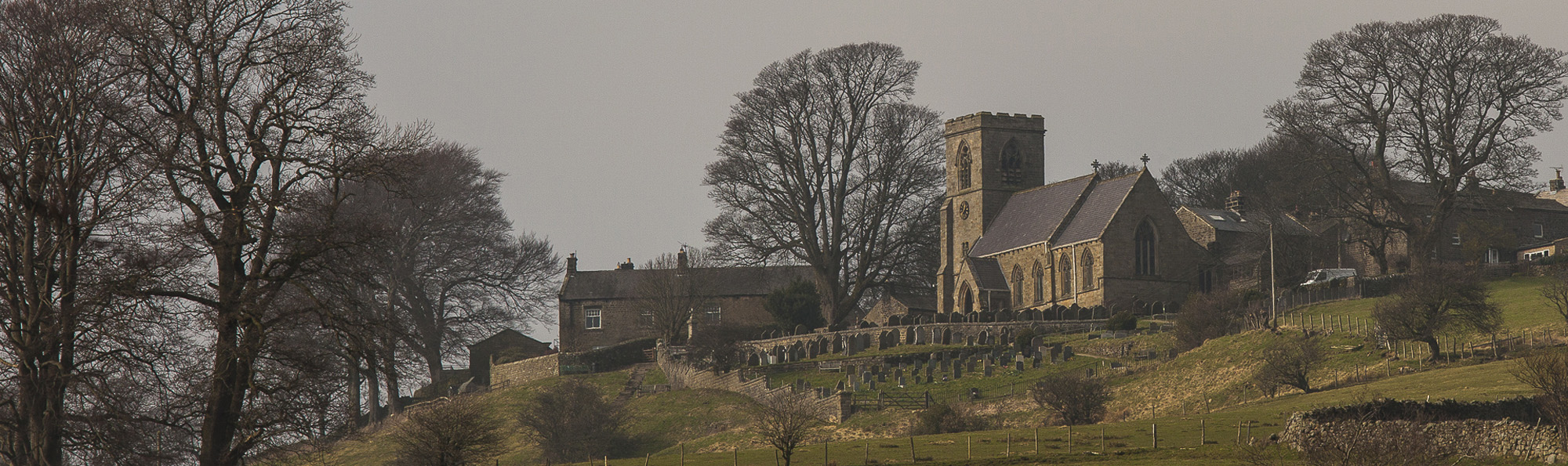 Looking up towards Middlesmoor church and graveyard with some bare winter trees and some houses around it