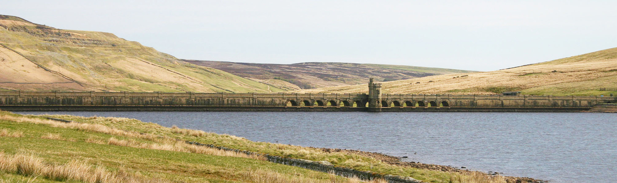 Water in reservoir with stone dam surrounded by grass covered hills