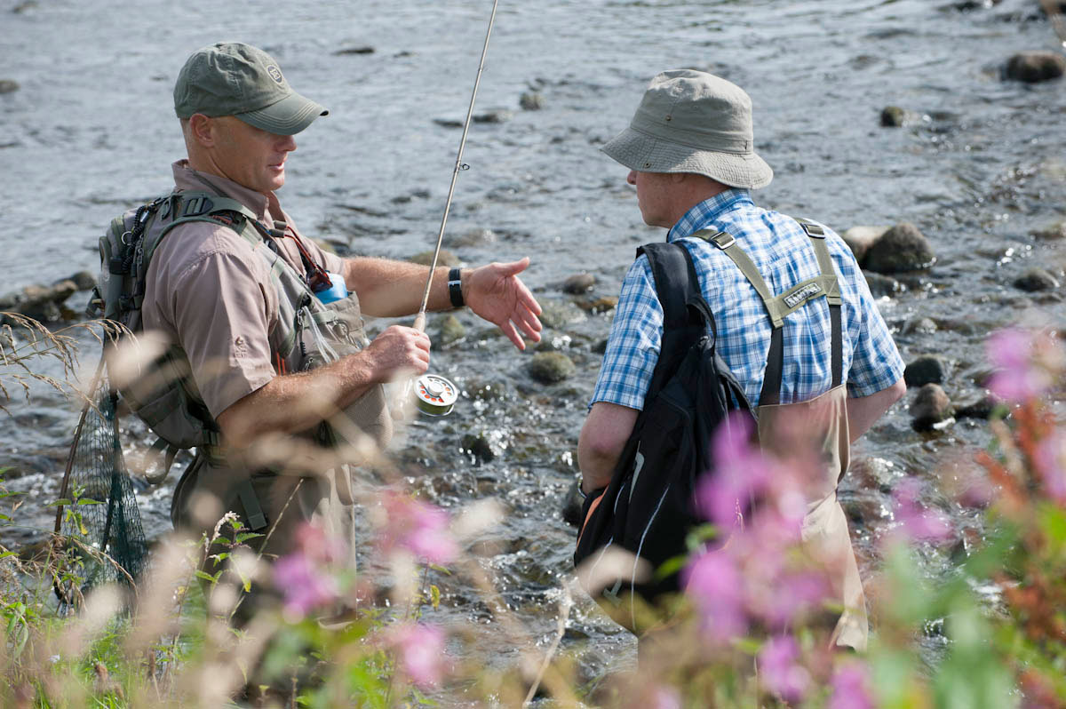 A close up of two fisherman talking whilst stood in some rocky water