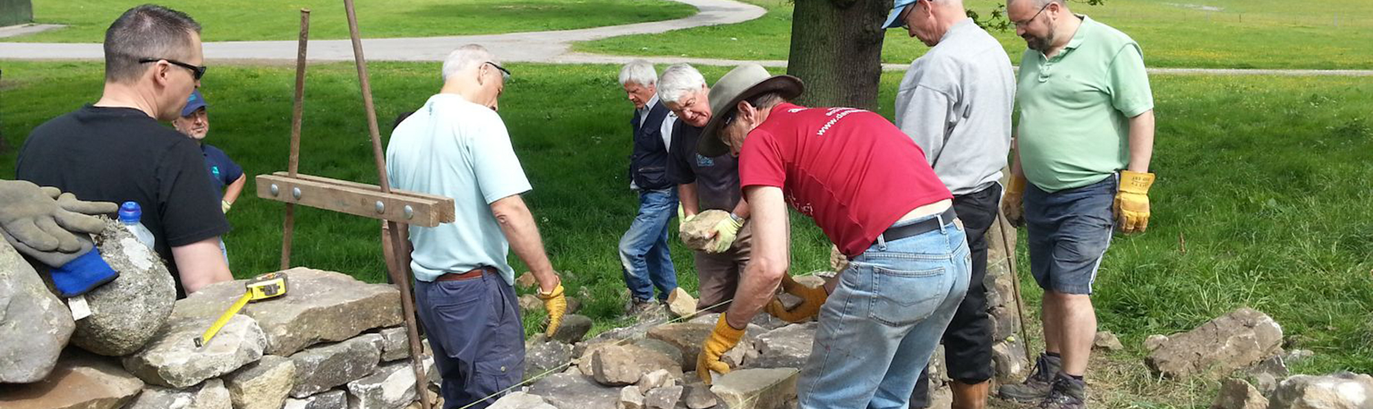 A group of 8 or 9 men stood around a section of dry stone wall being built