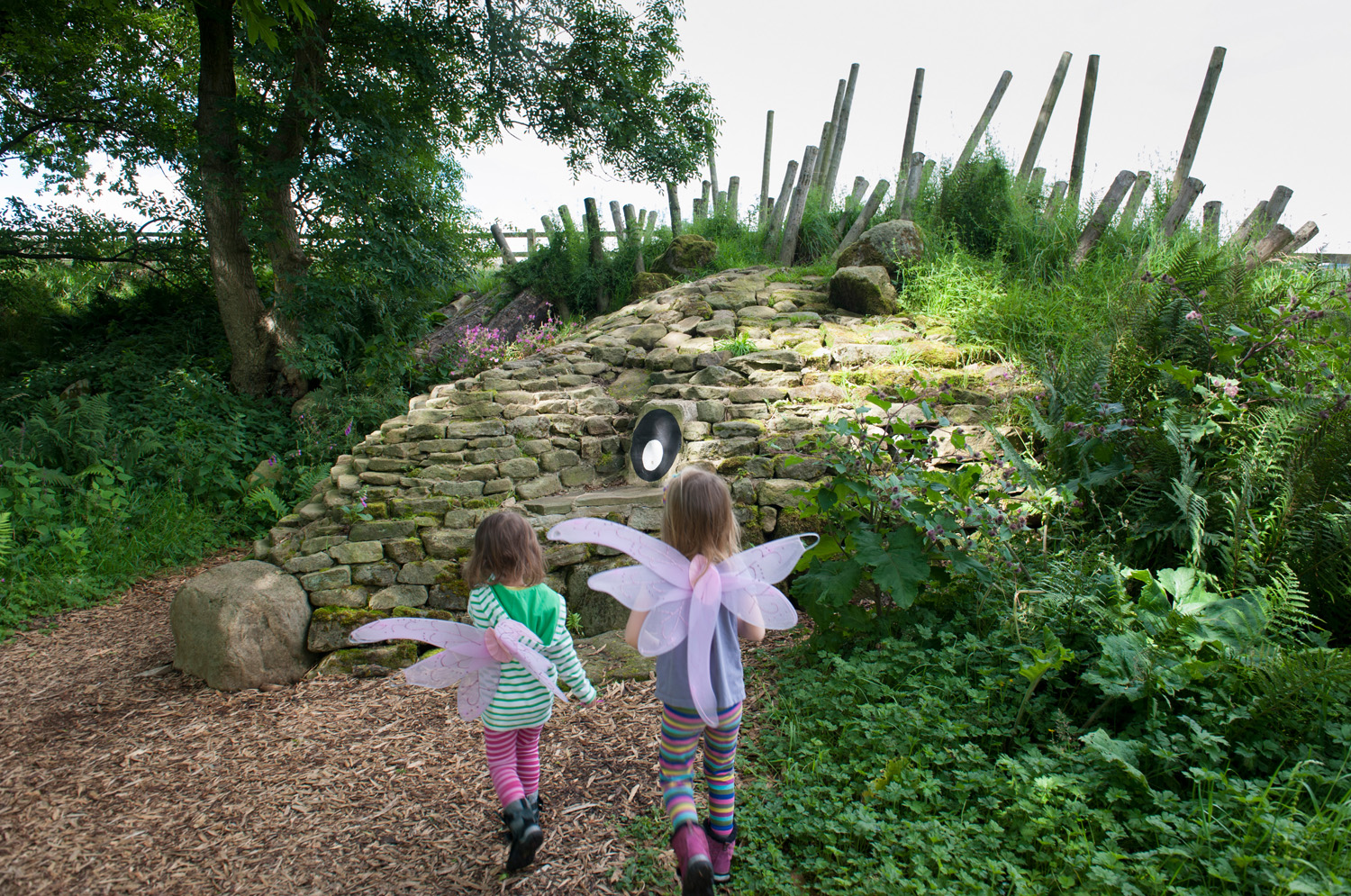 Two young children wearing fairy wings walking toward stone sculpture