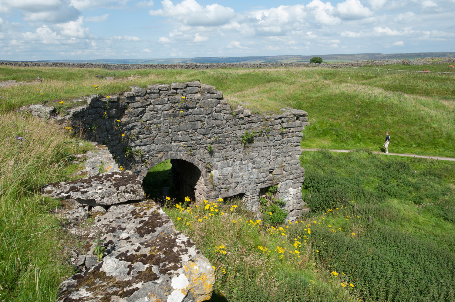 Stone ruins of a lime kiln surrounded by green grass
