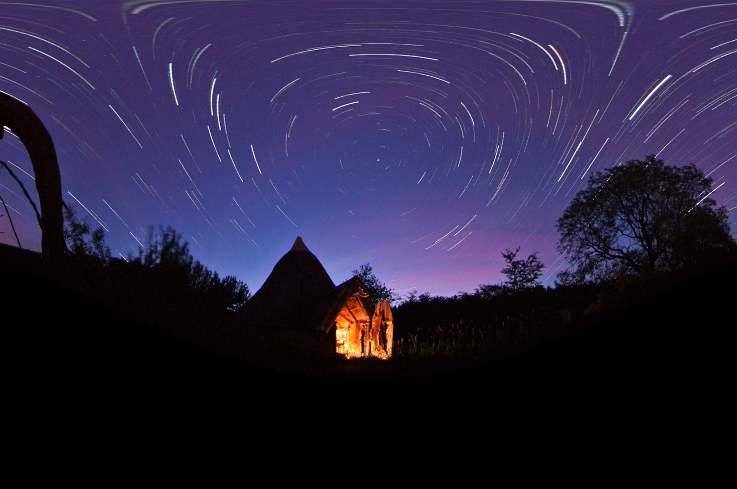 Dark sky with stars above small hut with light on inside
