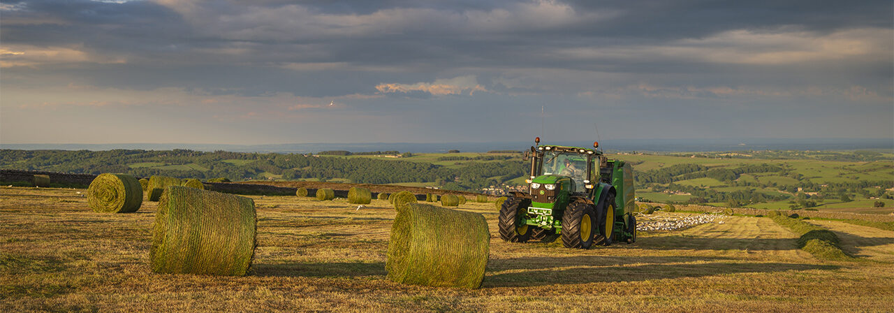 Green tractor and hay bales in field under dark clouds