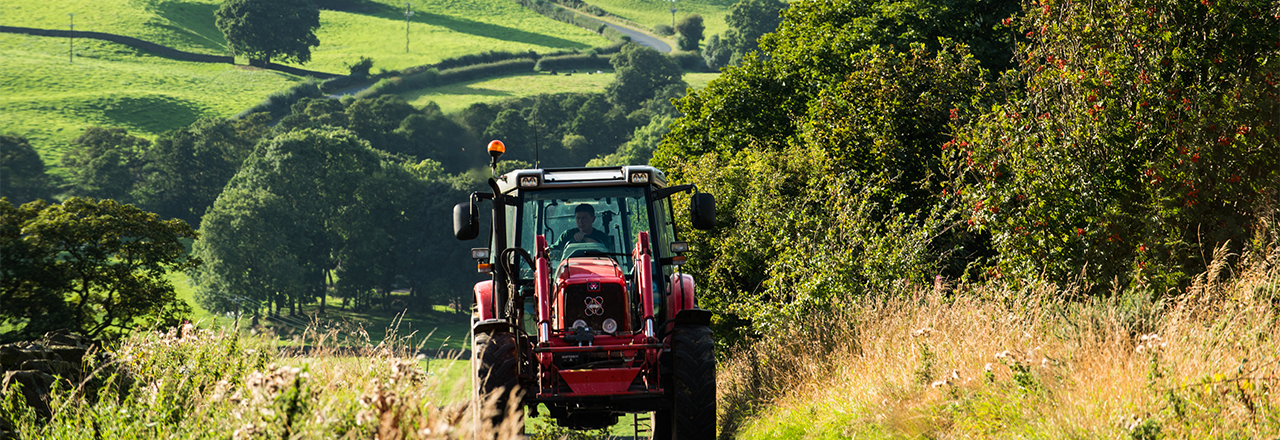 Red tractor driving up hill with green landscape in background